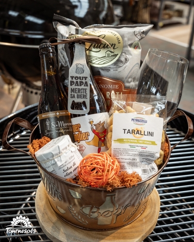 Panier garni pour la fête des pères avec bières, verre et snacks sur un barbecue.